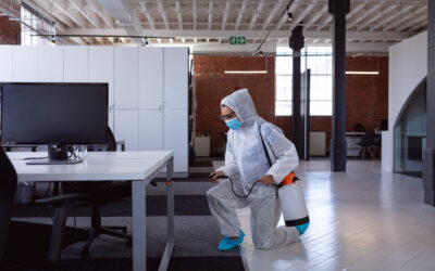 Cleaner wearing ppe suit, glasses and mask disinfecting office workspace. hygiene in business at a modern office during coronavirus covid 19 pandemic.